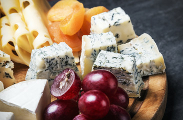 Cheese plate with fruits and nuts on a black background