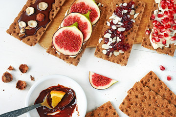 Set of crisp rye bread sandwiches with fig, cranberry jam and almond, soft cheese, chocolate paste and hazelnut over white background. Top view.