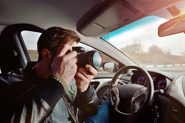 The photographer is driving a car. Beautiful guy with a photo camera. Examines photos in the car. The traveler photographs through the window