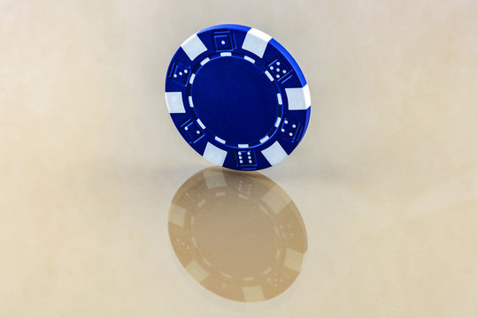 The blue casino chip stands on the reflecting surface