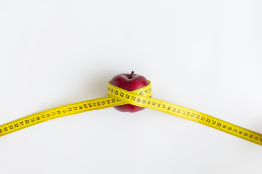 Dieting concept. Red apple with yellow measuring tape isolated on white