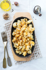 Baked cauliflower with spices and garlic in a cast-iron frying pan on a light background. Selective focus.Top view.