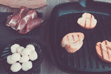 Toast bread on grill pan near plate with mozzarella and ham. Toned photo. Bruschetta ingredient.