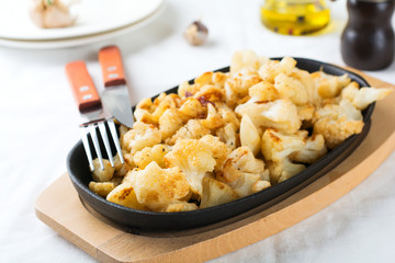Baked cauliflower with spices and garlic in a cast-iron frying pan on a light background. Selective focus.