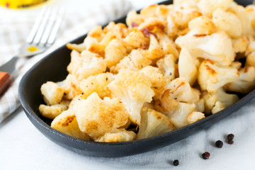 Baked cauliflower with spices and garlic in a cast-iron frying pan on a light background. Selective focus.
