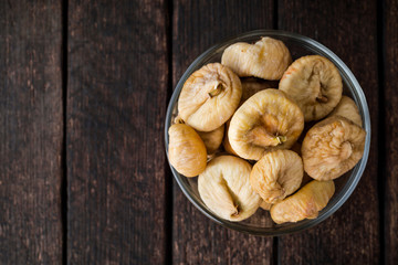 Dried figs in glass bowl on wooden background.