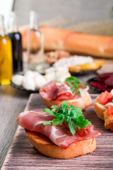 Bruschetta with prosciutto and arugula on wooden background.