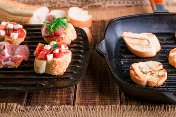 Set of bruschetta on black grill pan on wooden background. Tasty antipasto.