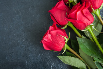 Three red roses over black stone background. Copy space. Close up.