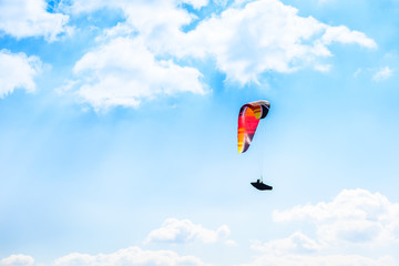Paraglider flying against the blue sky with white clouds.