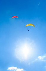 Two paragliders flying against the blue sky with white clouds.
