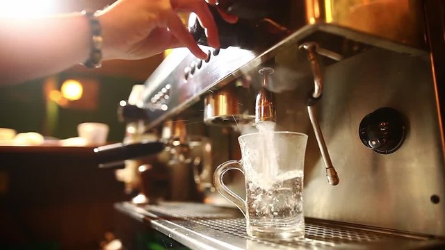 Dolly shot of a barista pouring some boiled water in a transparent cup, in a bar.