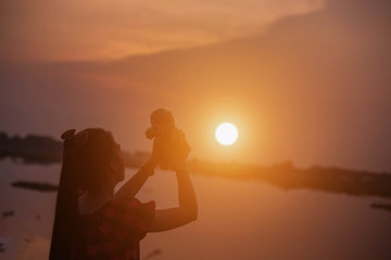 Woman holding a teddy bear in sunset 