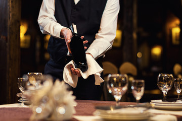 The waiter offers visitors wine,Waiter in uniform waiting an order,Waiter with a white towel on his hand,Confident waiter,A pub.Restaurant.Classic.Evening.European restaurant