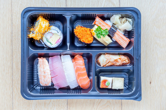 Top view of bento to-go plastic box, mixed nigiri and assorted sushi roll in lunch box.