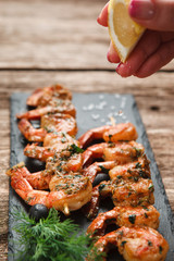 Preparing Japanese seafood master class. Hand squeezing lemon on appetizing fried shrimps served on black slate, close up view.