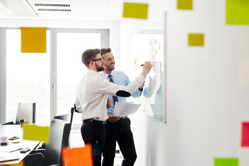 Two businessmen working at office planning new strategy on whiteboard
