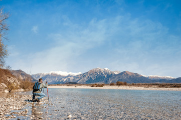 Fototapeta premium Mature hiker on the bank of a river. Walking toward mountain.