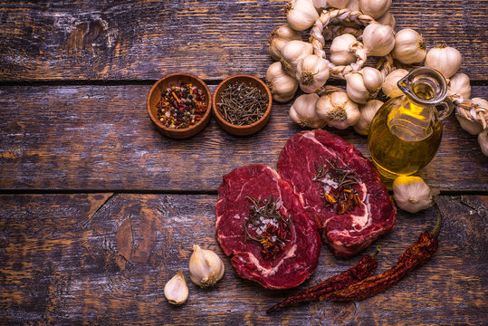 Raw Beef Steak, salt, pepper, garlic, rosemary, olive oil  on the black wooden board, background.