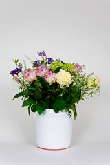 Bouquet of flowers in a white vase against a white background.