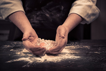 The chef breaks eggs into a flour on a wooden table