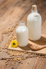 A bottle of soy milk or soya milk and soy beans on wooden table.