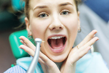 Closeup portrait young terrified girl woman scared at dentist visit, siting in chair, screaming, opened mouth, doesn't want dental procedure drilling tooth extraction isolated clinic office background