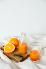 Orange fresh for breakfast in a glass and in a bottle with a straw. On the wooden board lies an orange and a magazine. Healthy breakfast in bed, daylight, vertical shot.