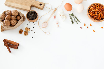 Vegetables, nuts, beans, cinnamon, rosemary, chicken eggs, other food and kitchen appliances lie on a white background. Space for text, daylight, horizontal image.