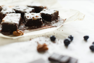 Table setting, chocolate dessert brownie cake with berries on parchment paper on a table covered with a linen tablecloth. Horizontal shot, daylight.