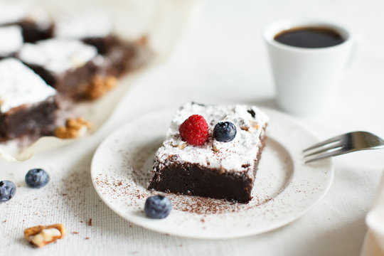 Table setting, coffee and chocolate dessert brownie cake with berries on a white plate on a table covered with a linen tablecloth. Horizontal image, daylight.
