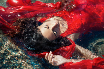 beautiful young woman in red dress laying dowm in water