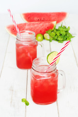 Cold watermelon lemonade / watermelon juice in mason jars with red striped straw, watermelon slices, mint and lime on a white table. Selective focus.