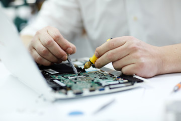 Closeup shot of male hands  working on disassembled laptop with screwdriver and tweezers looking...