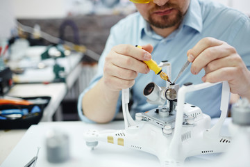 Closeup shot of man working on assembling new surveillance system using quadcopter drone with  action camera on table with different tools in modern workshop