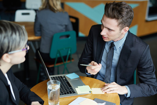 Young handsome HR manager sitting at cafe table and taking notes while conducting interview with female applicant for position