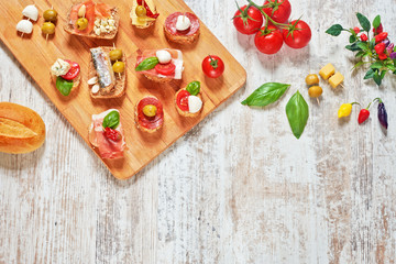 Mix of appetizers / snacks. Mediterranean tapas or antipasti on a rustic wooden table. Sandwiches with salami, jamon, sardines, salmon, mozzarella, cheese, tomato, olives, pepper, basil. Copy space.