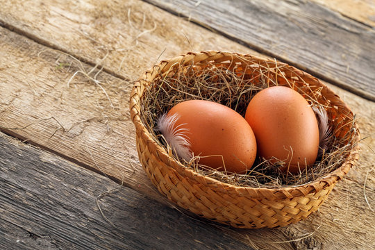 Two fresh farm chicken eggs in a rustic basket on a wooden table. Close-up shot. Top view.