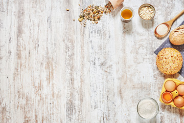 Baking background. Set of fresh bread, wholegrain flour, olive oil, eggs in a carton tray, wooden spoon, grains and seeds over light wooden table. Copy space.