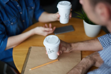 Close-up shot of young HR manager sitting at cafe table, drinking delicious coffee and conducting interview with female applicant for position