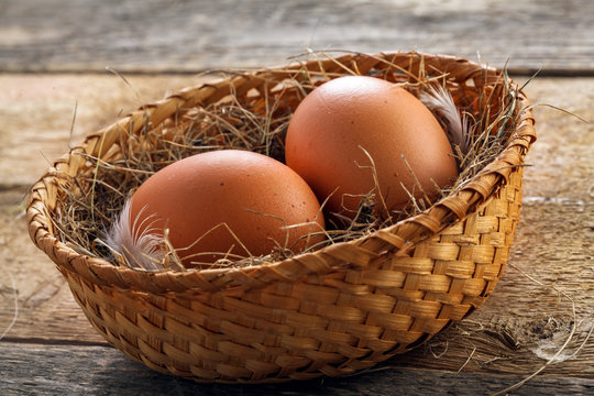 Two fresh farm chicken eggs in a rustic basket on a wooden table. Close-up shot.