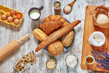 Baking background. Set of fresh bread, wholegrain flour, eggs, grains and seeds, oat flakes, olive oil, milk, wooden board, spoon, rolling pin on a light rustic table.