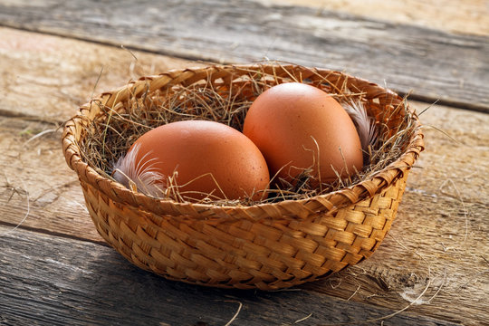 Couple of big chicken eggs in a basket on a wooden background. Close-up shot.