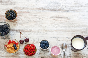 Summer breakfast / country meal background. Cup of milk, fresh seasonal berries, cornflakes and yogurt on a rustic wooden table. Space for text.