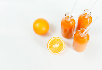 Three bottles of orange juice and tubes are on the table on a white background, as much as two oranges and one orange cut into wooden Boards. Daylight, horizontal image.