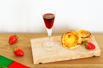 Symbols of Portugal: Portuguese flag, porto wine and pasteis de nata (custard tart) on a wooden board. 