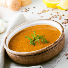 Lentil soup in a rustic bowl with piece of bread on a cotton canvas tablecloth. Healthy vegetarian food on a white wooden table.