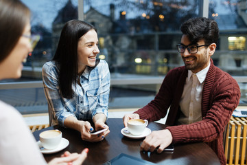 Carefree friends or colleagues talking by cup of coffee in cafe