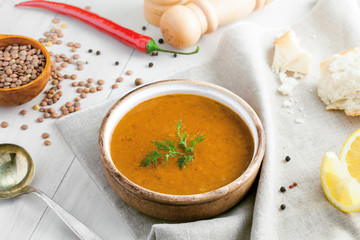 Lentil soup in a rustic bowl and a piece of bread on a cotton canvas tablecloth. Healthy vegetarian food on a white wooden table.