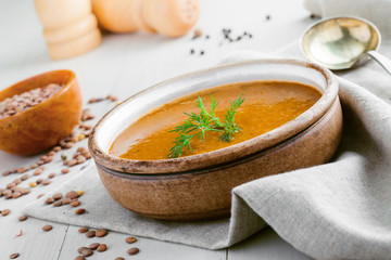 Delicious soup made of lentils in a rustic clay bowl served on a canvas tablecloth. Healthy vegetarian meal on a table. Close-up shot.